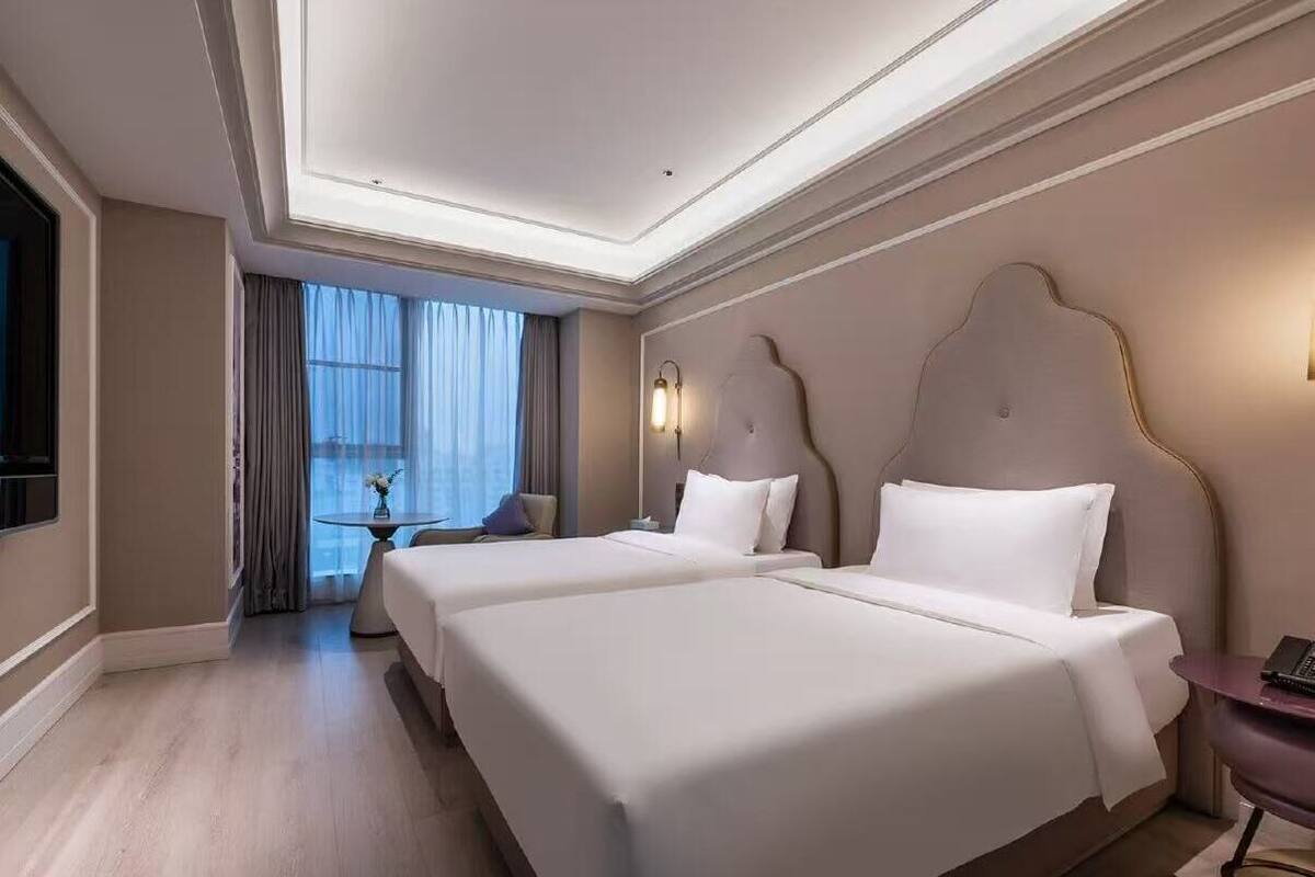 A hotel room with two beds, a flat-screen TV, a round table, and a large window with curtains.