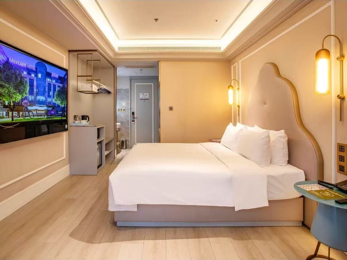 A modern hotel room with a large bed, a TV, a desk, and a bathroom.