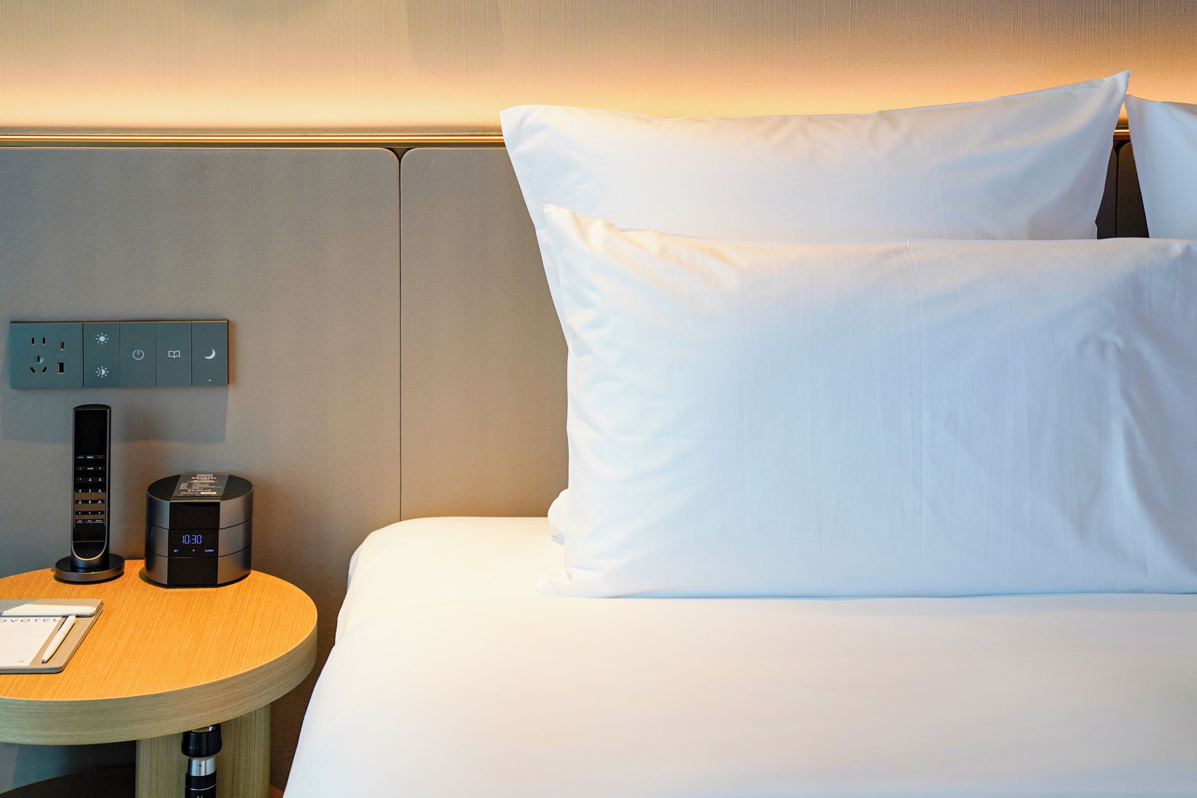 Une chambre d’hôtel équipée d’un lit, d’oreillers, d’une table de chevet avec une horloge et d’une prise électrique.