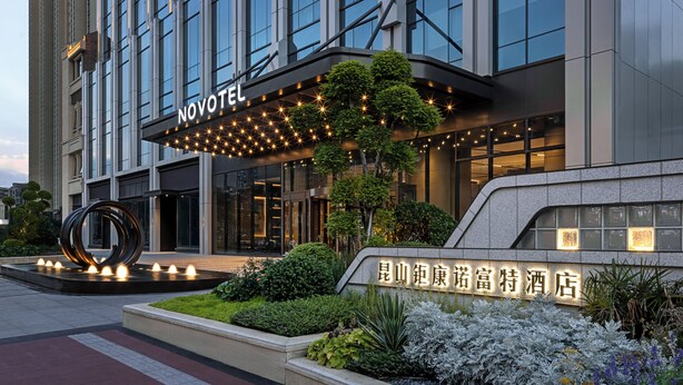 A hotel with a modern facade, a prominent 'NOVOTEL' sign, and a landscaped entrance area. - Novotel Kunshan East (Suzhou)