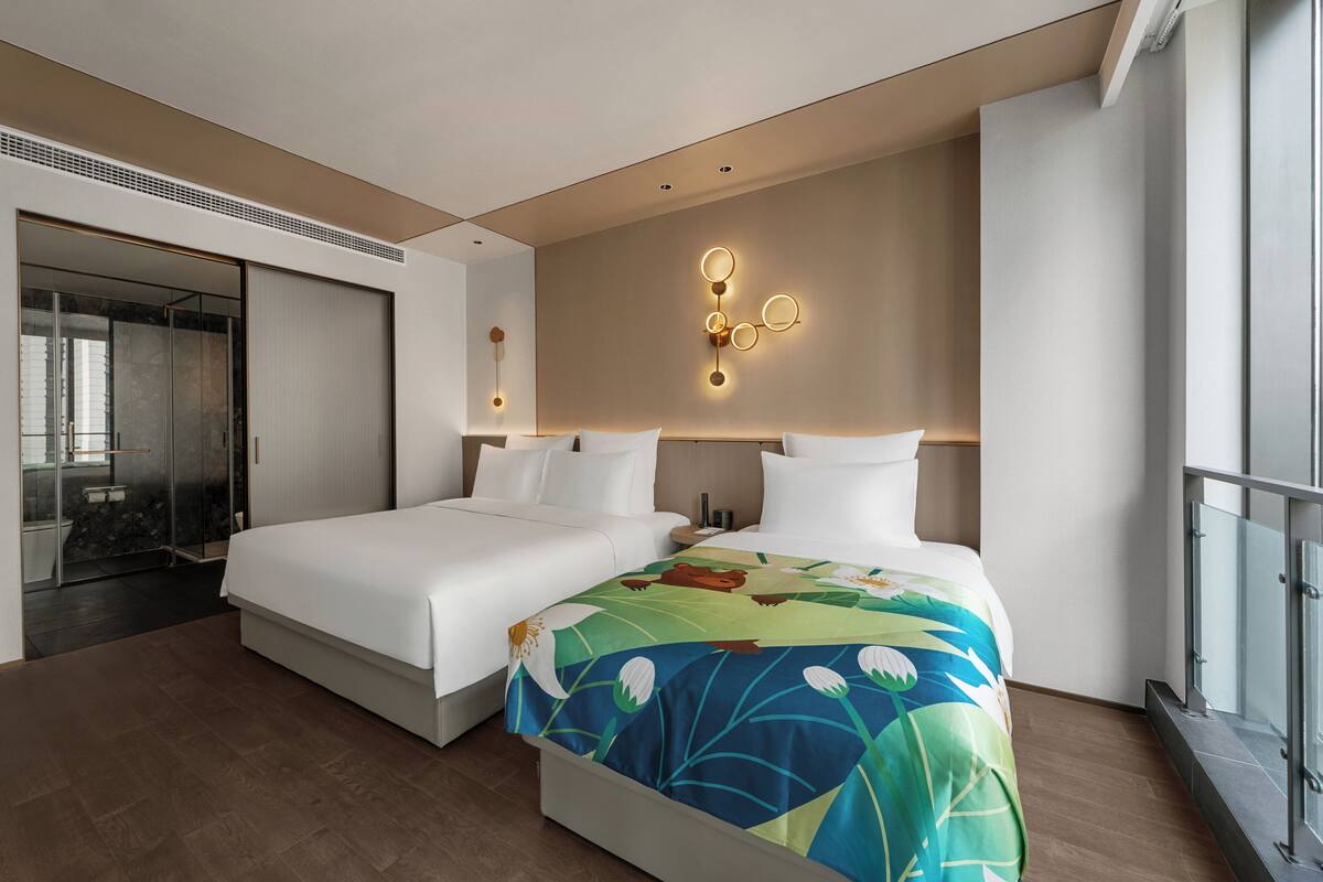 A modern hotel room with two beds, a large mirror, a sliding door, and a wall-mounted light fixture.