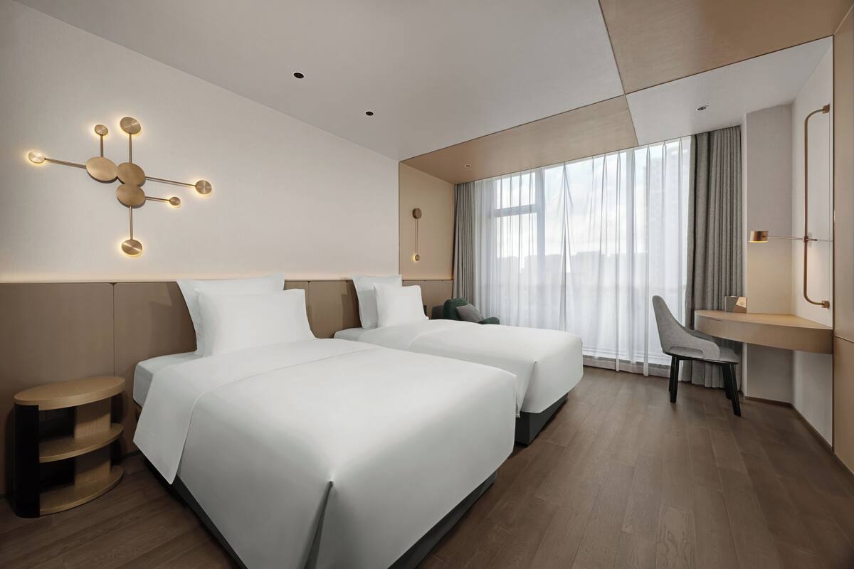 A modern hotel room with two beds, a desk, and a large window with curtains.