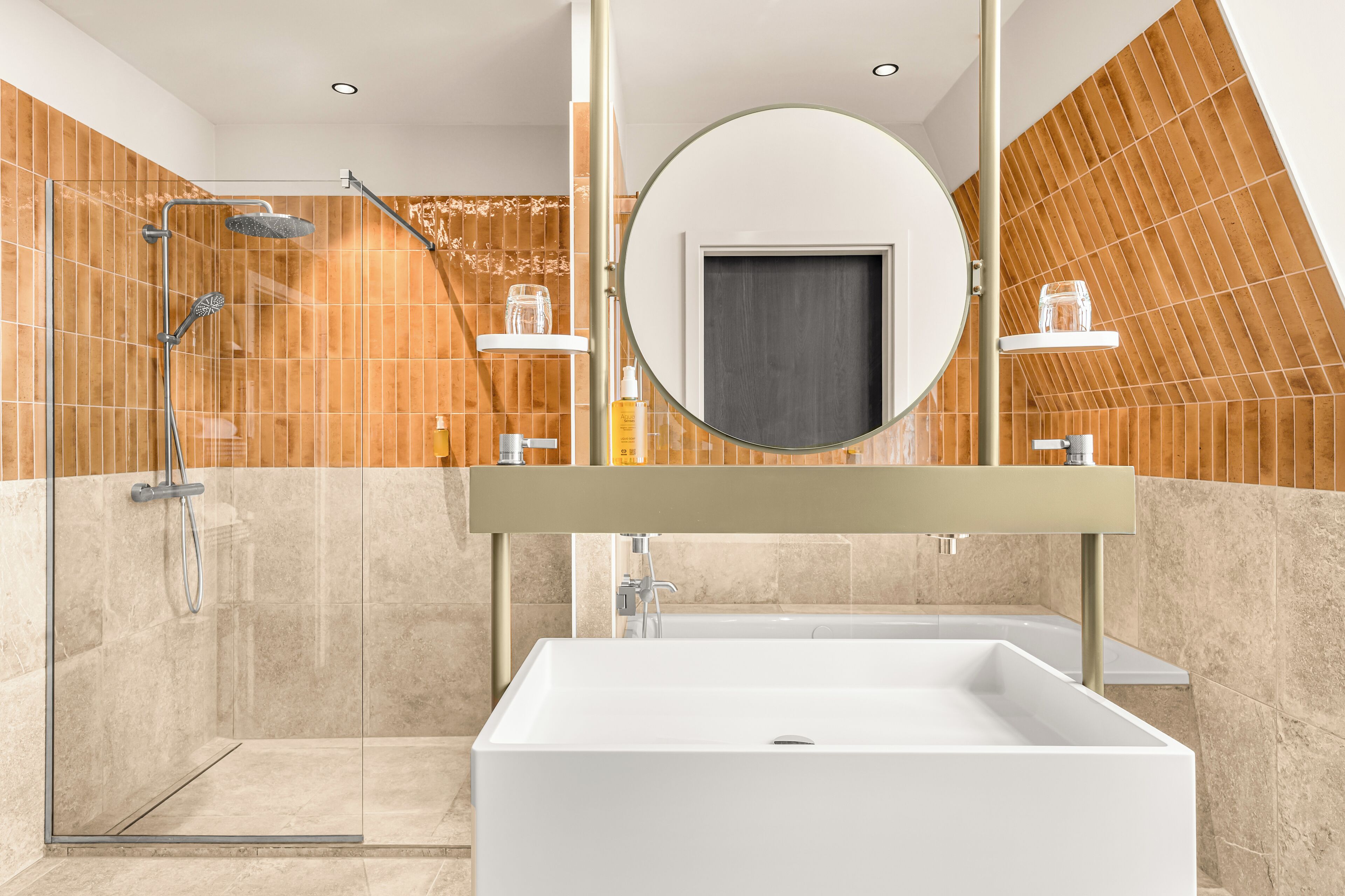 Un bany modern amb dutxa de vidre, una banyera rectangular gran i un mirall rodó sobre un lavabo amb prestatge de fusta.