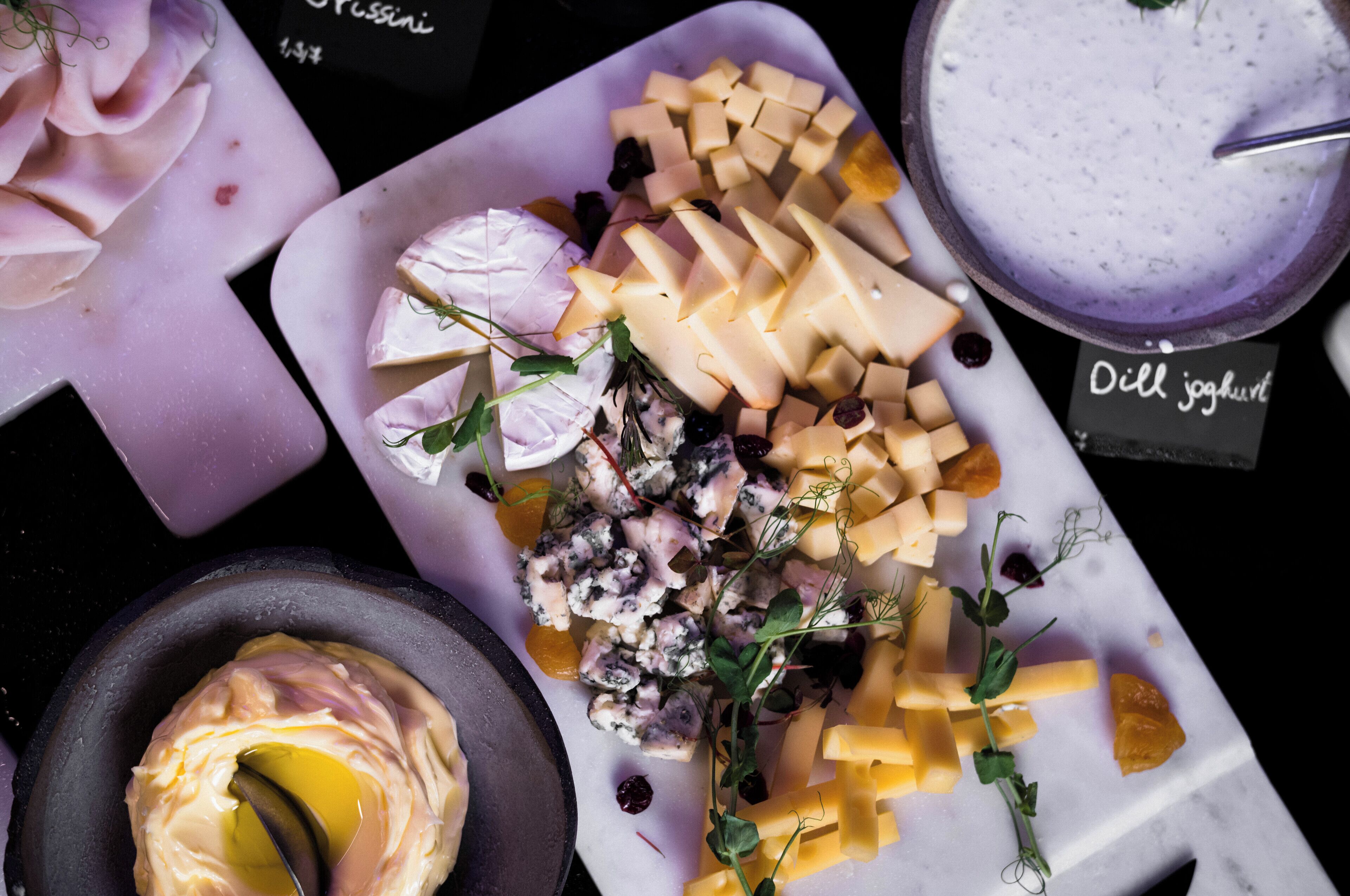 A variety of cheeses and a bowl of yogurt on a marble surface.