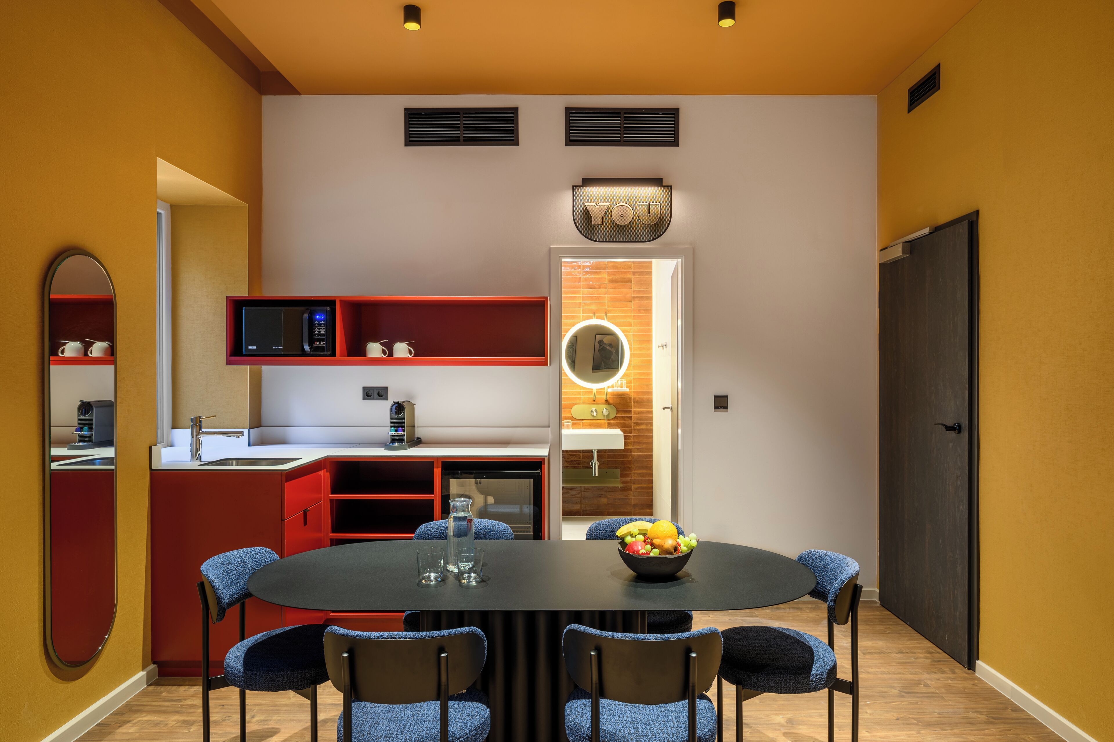 A modern kitchen with a dining area, featuring a round table with chairs, a microwave, and a red cabinet.