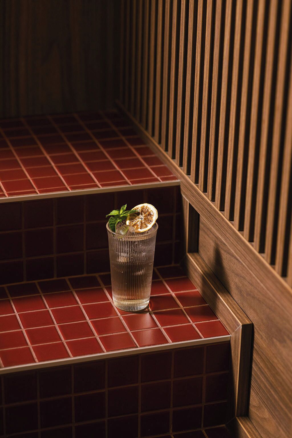 A glass with a mint garnish on a red-tiled step.