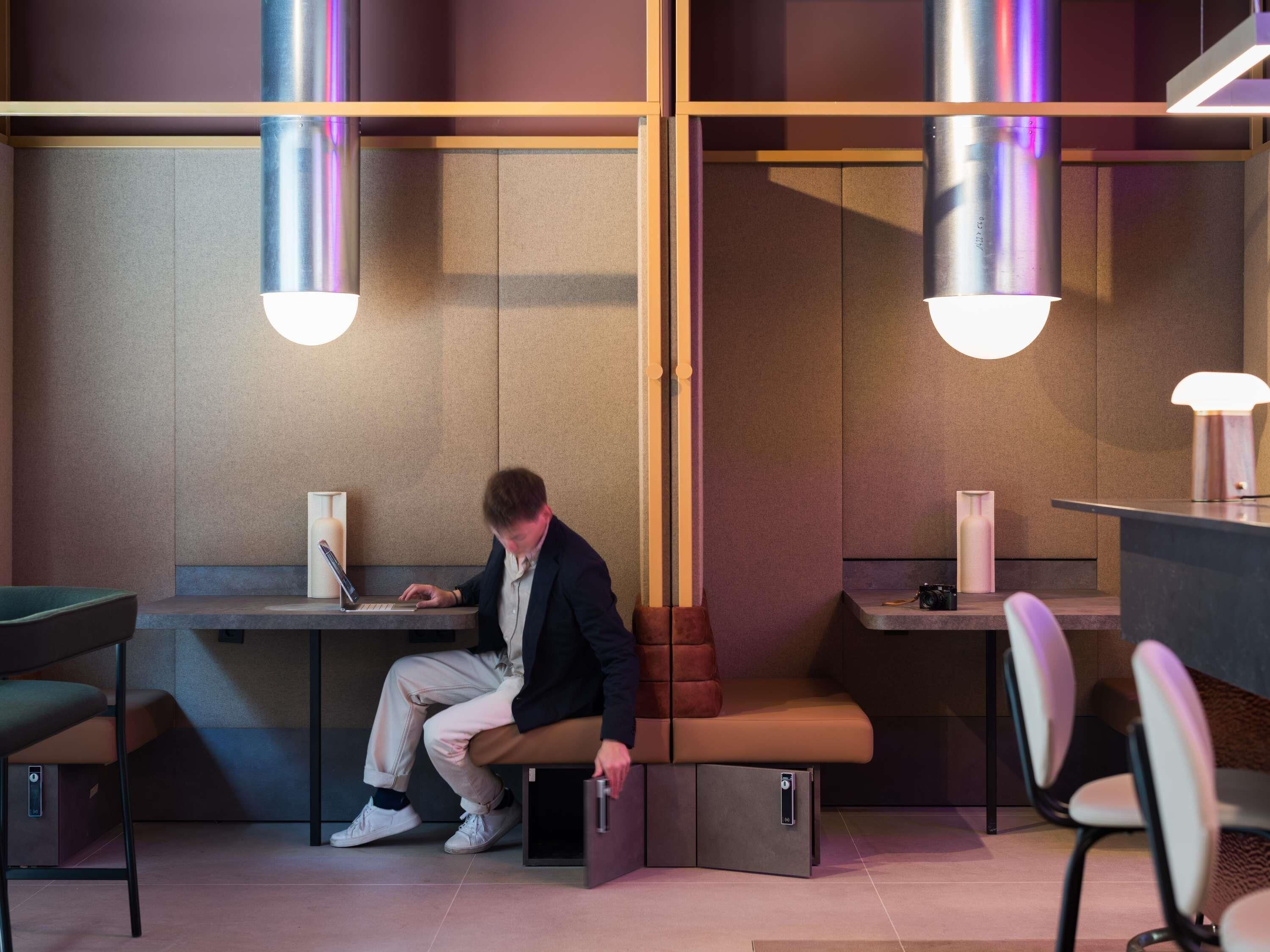 A modern office space with a person working at a desk, a bench, and a small table with a camera.