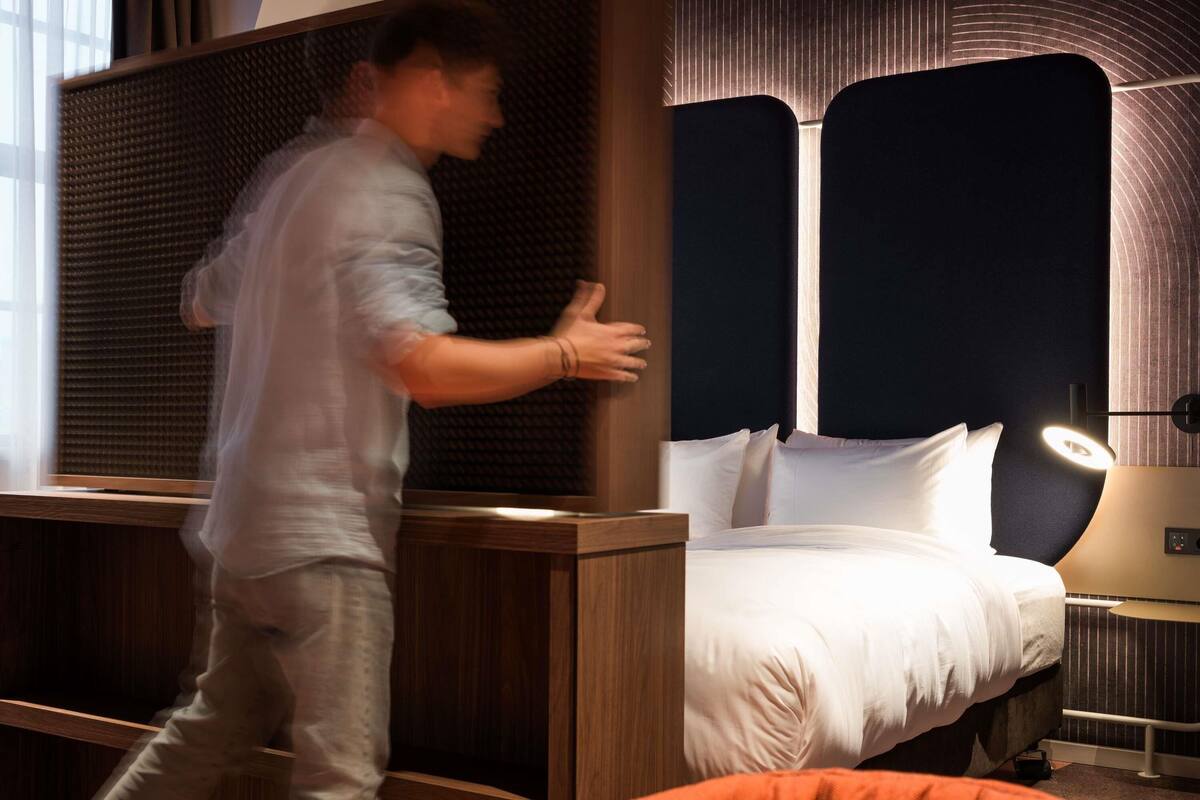 A hotel room with a bed, a nightstand, a lamp, and a window with blinds.