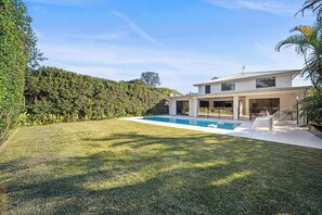 Una casa moderna con piscina, un porche cubierto y un césped verde exuberante.