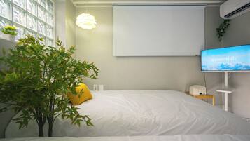 Une chambre à coucher avec un lit, une plante en pot, une table de chevet avec une lampe et un téléviseur fixé au mur.
