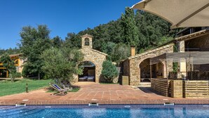 A stone building with a bell tower, a swimming pool, and a covered outdoor seating area.