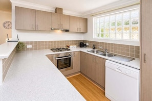 A modern kitchen with wooden cabinets, a built-in oven, a dishwasher, and a window with a view of greenery.