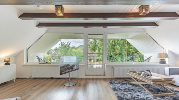 A modern loft bedroom with a large skylight, wooden flooring, and a cozy seating area. - Vacation apartment "Heimathafen" in Breklum for up to 4 people (Breklum)