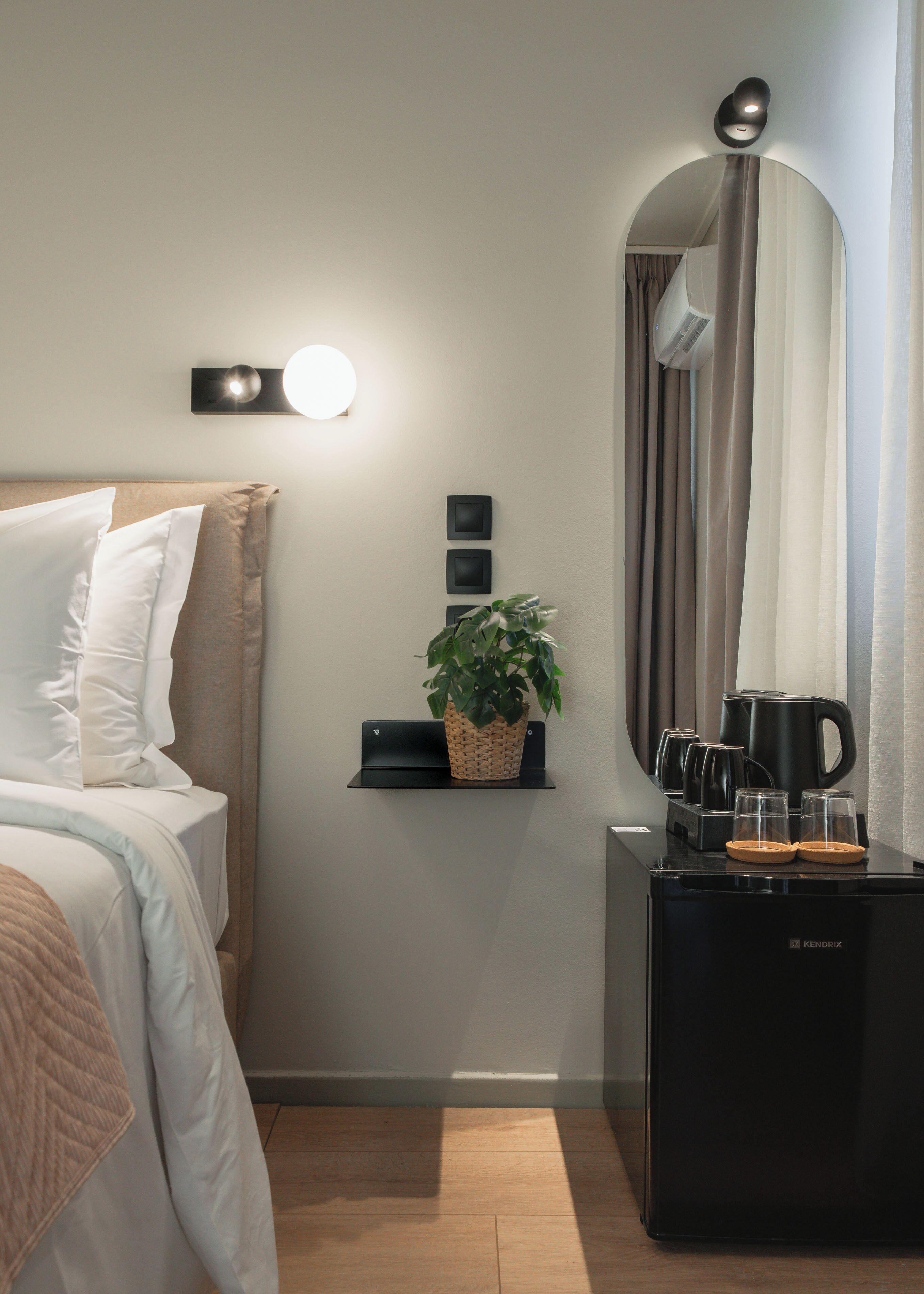 Una habitación de hotel con una cama, un estante pequeño con una planta, un espejo, una cafetera y un hervidor.
