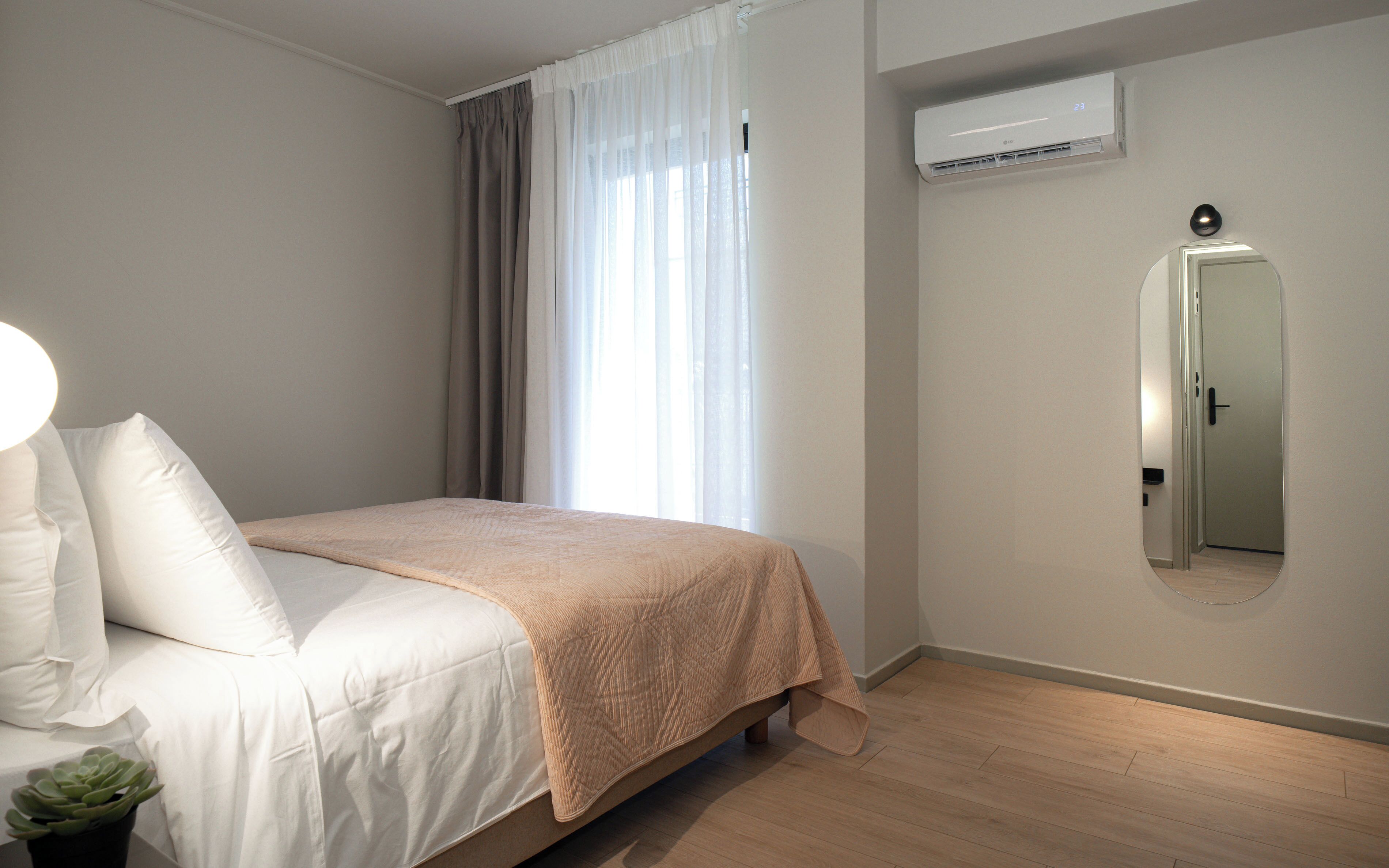 A bedroom with a bed, a potted plant, a mirror, and an air conditioning unit.