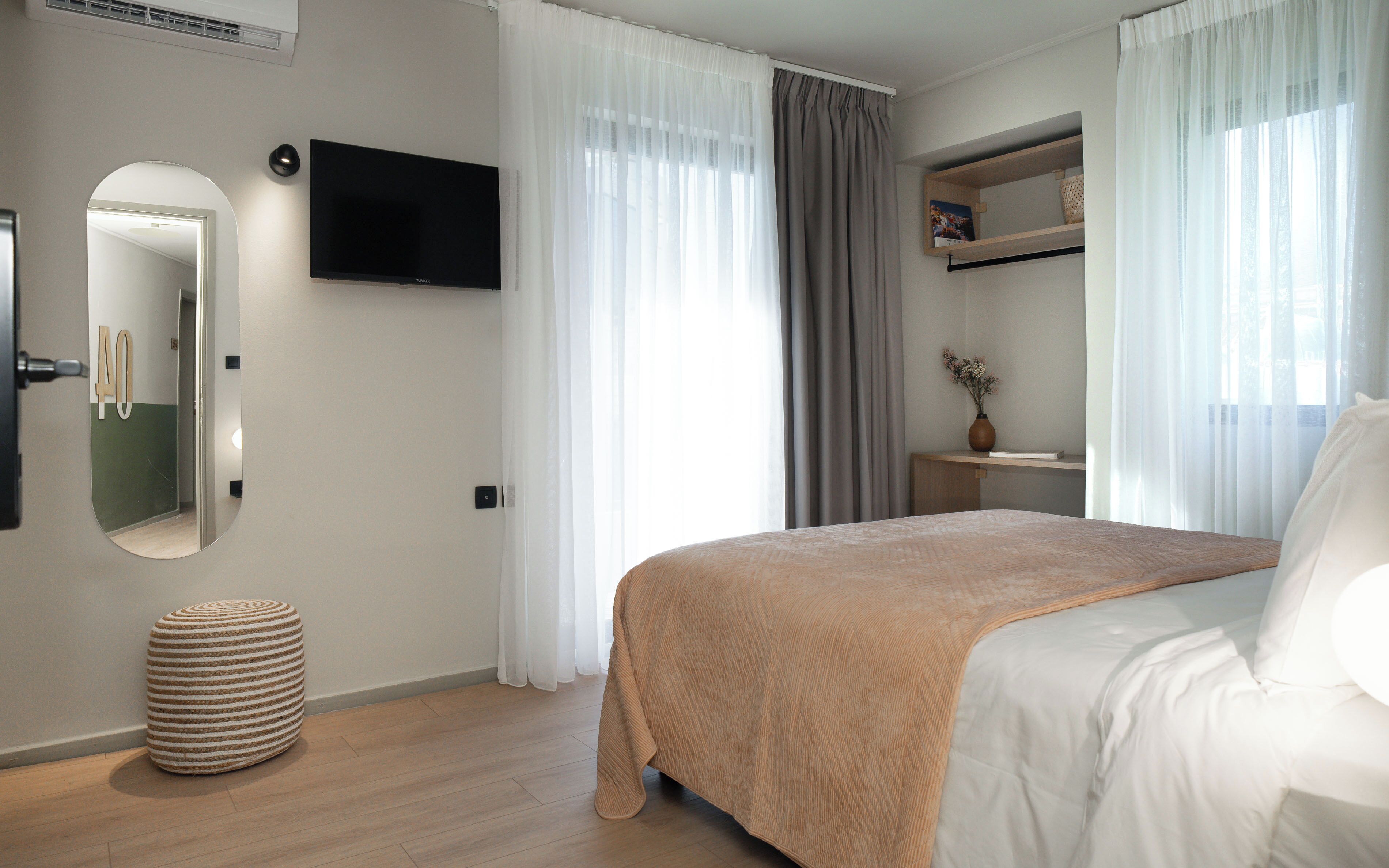 A bedroom with a bed, a TV mounted on the wall, a small table with a vase, and a mirror.