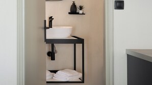A modern bathroom with a white sink, black fixtures, a round mirror, and a small shelf with a plant. - Gnamma Hotel (Palaio Faliro)