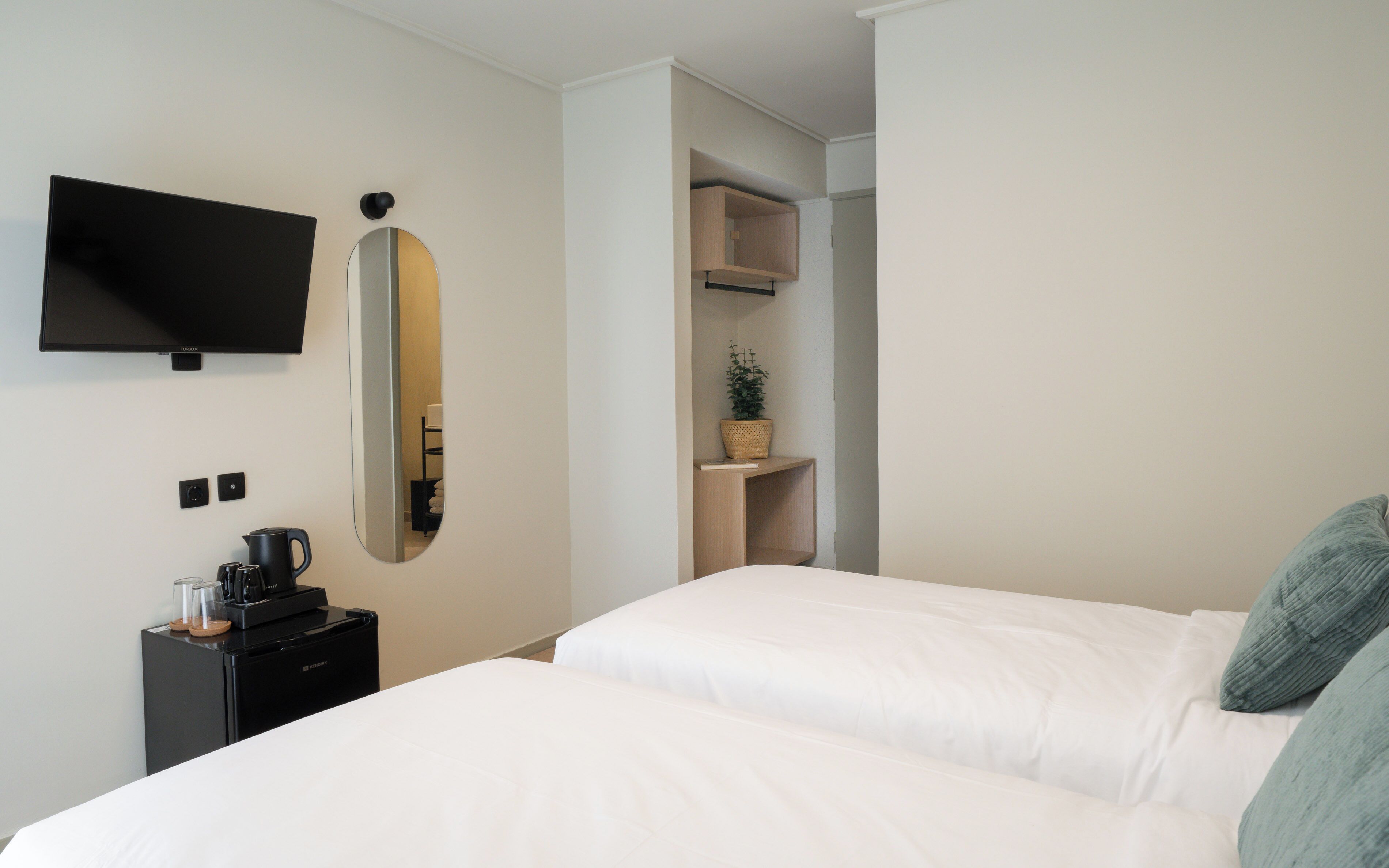 Hotelkamer met een bed, een televisie, een koffieapparaat, een spiegel en een plank met een plant.