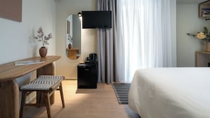 A hotel room with a bed, a desk with a chair, a coffee maker, a mirror, and a television. - Gnamma Hotel (Palaio Faliro)