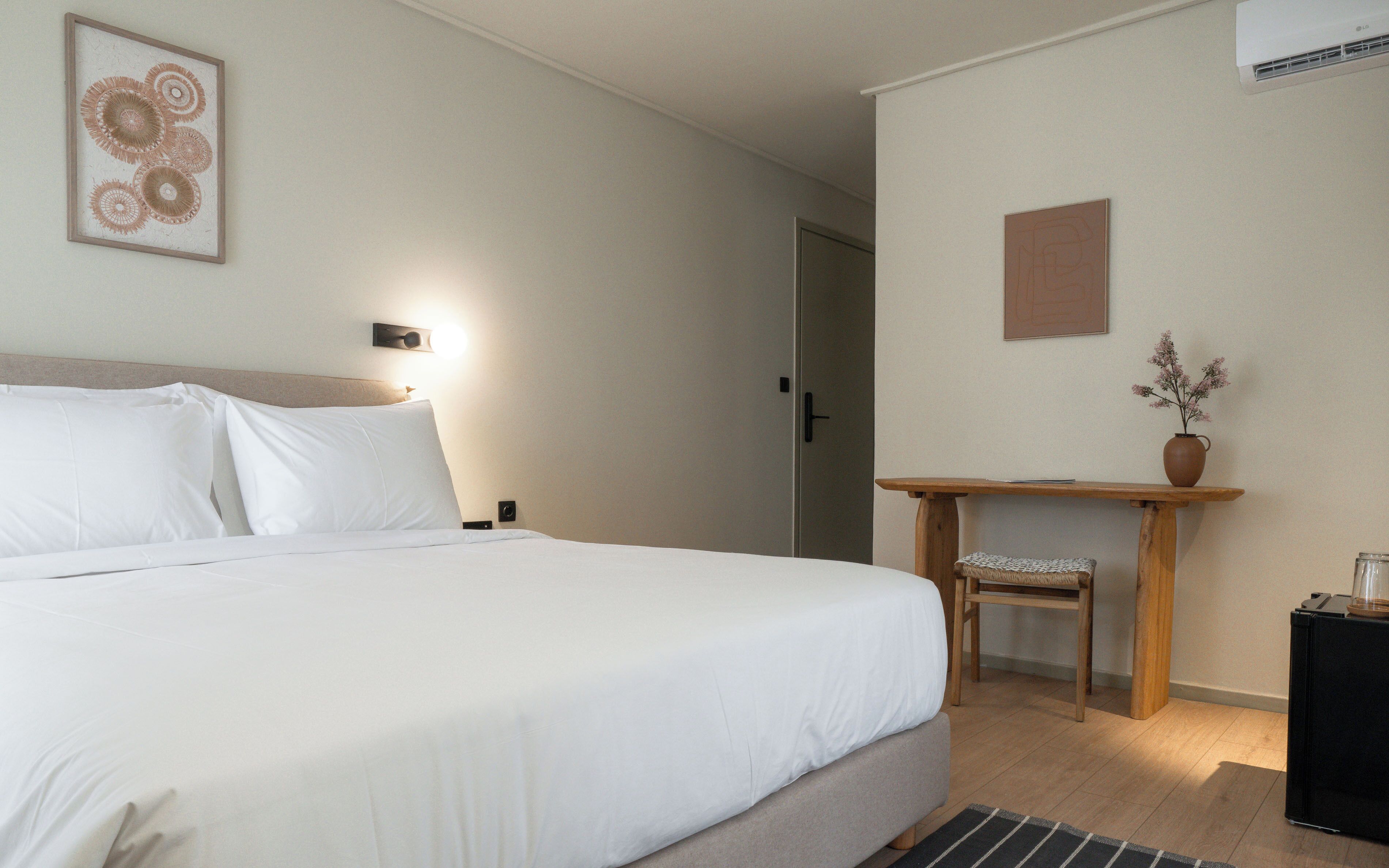 A neatly made bed with white linens, a bedside table with a vase of flowers, and a small wooden stool.