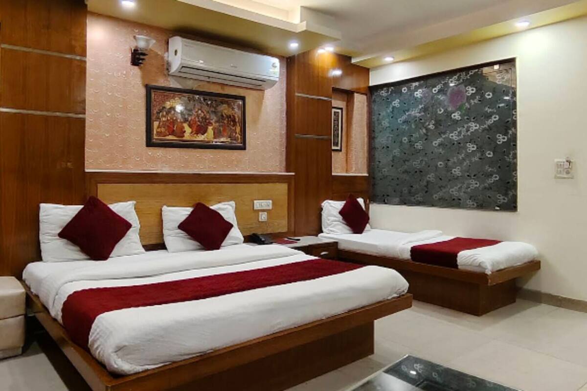 Quarto de hotel com duas camas, uma janela grande com cortina estampada, ar condicionado e uma obra de arte pendurada na parede.