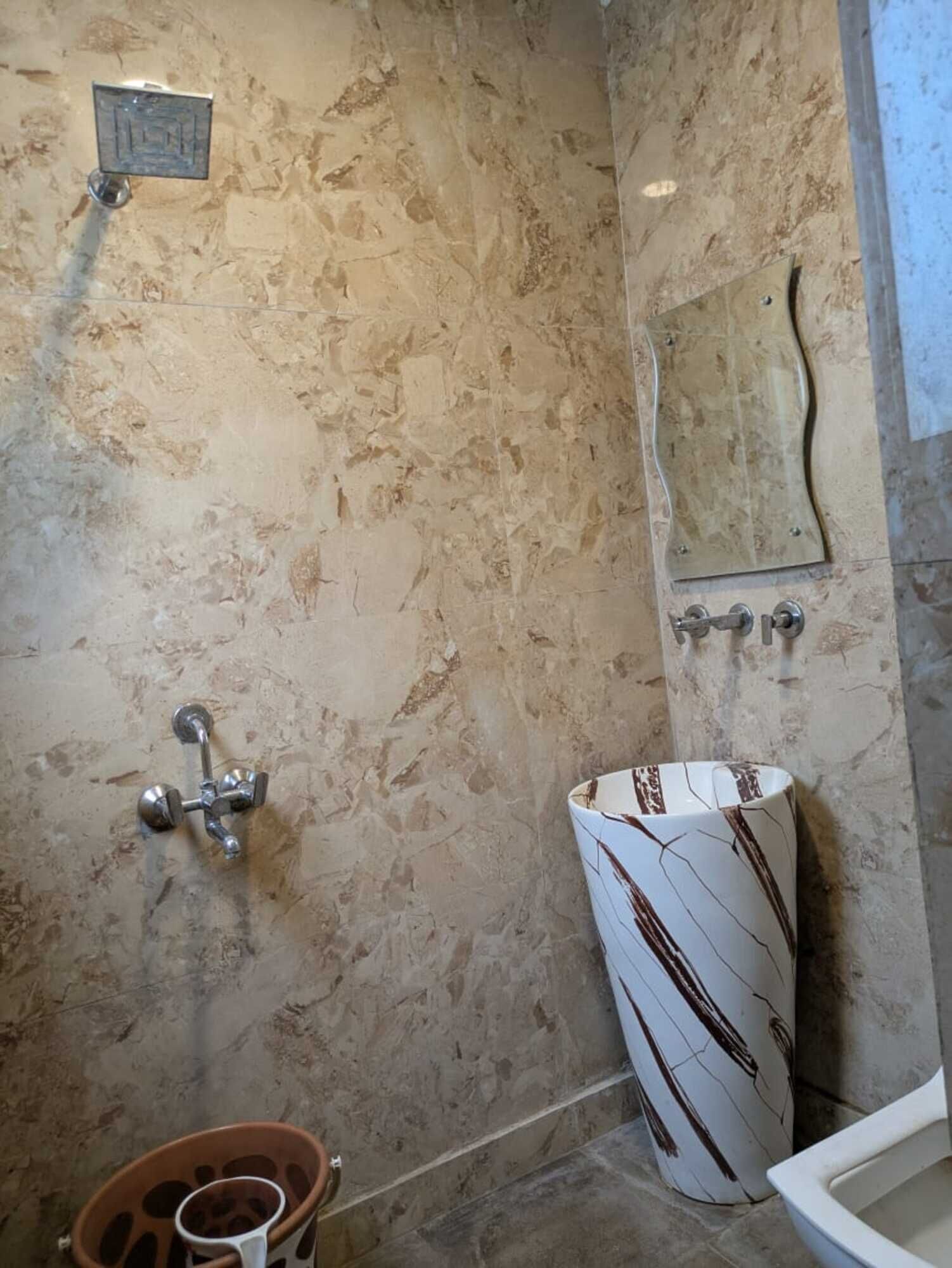 A bathroom with a marble wall, a white sink with a unique design, and a shower area.