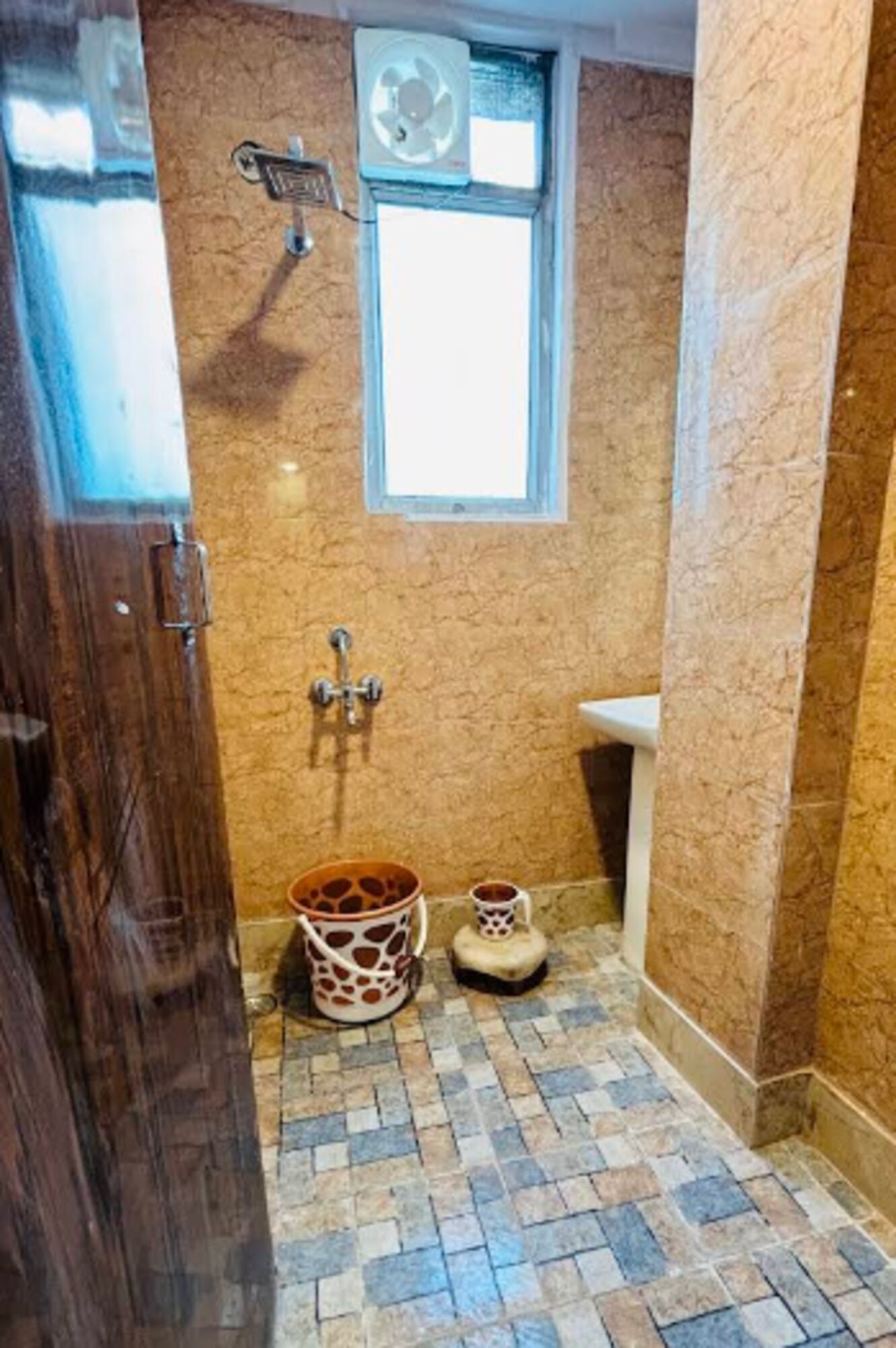 A bathroom with a stone-patterned floor, a window, a wall-mounted fan, and a small sink.