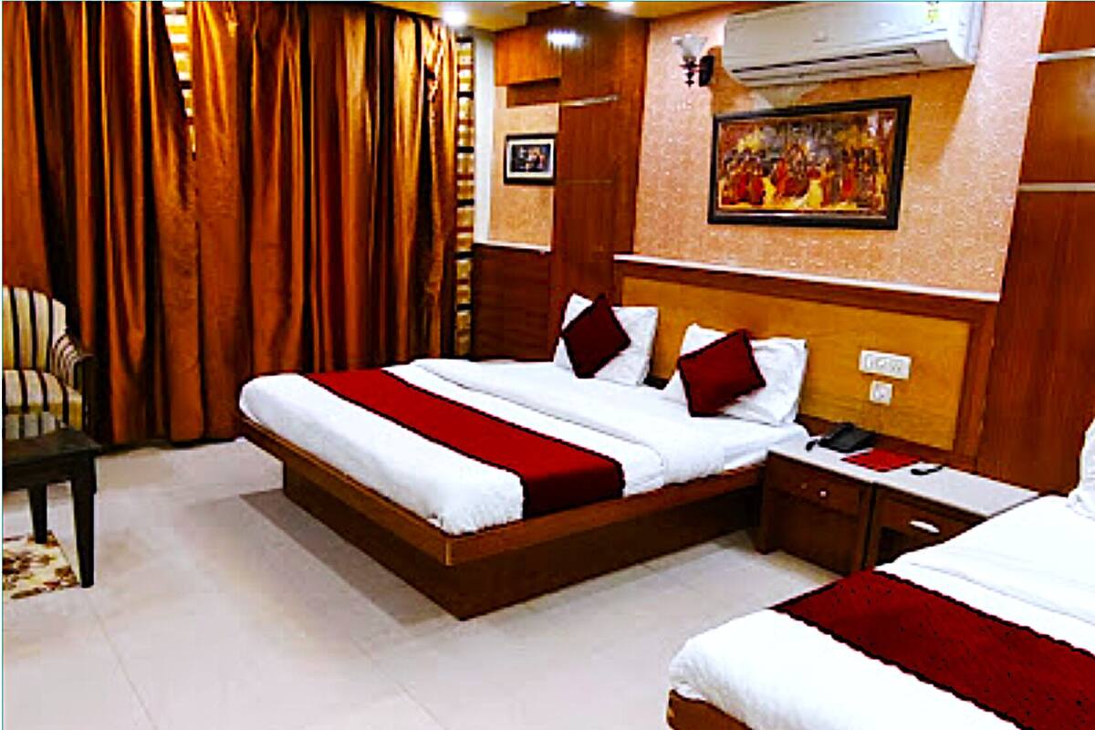 Quarto de hotel com uma cama grande, uma cama menor, uma mesa de cabeceira, uma cadeira e um quadro na parede.