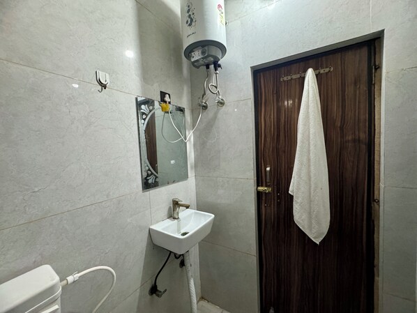 A bathroom with a white sink, a mirror, a towel hanging on the door, and a water heater mounted on the wall. - Hotel Bhavna Bhawan 800 m from Prem Mandir (Vrindavan)