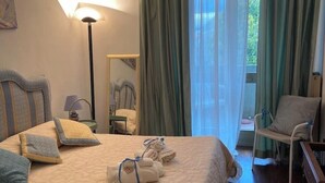 Een hotelkamer met een bed, een bedlampje, een stoel, een raam met gordijnen en uitzicht op groen.