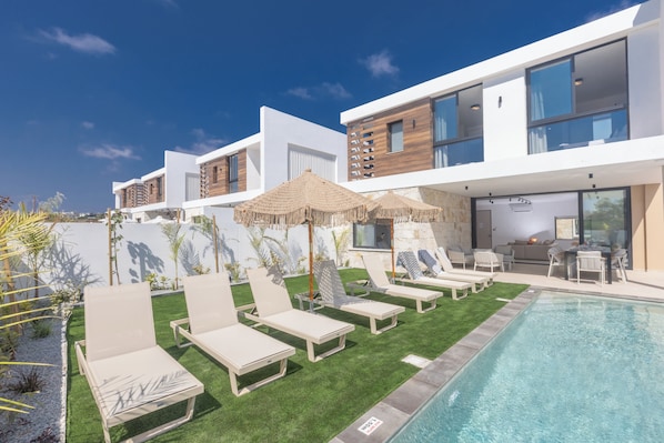 A modern hotel with a pool, lounge chairs, and a dining area.