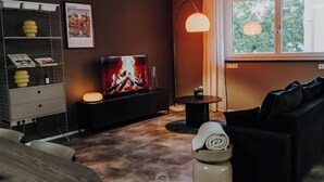 Een moderne woonkamer met een flatscreen televisie, een open haard, een bank, een salontafel en een raam met uitzicht op bomen.