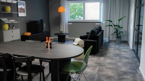 Een moderne woonkamer met een eettafel, stoelen, een bank, een televisie en een potplant.