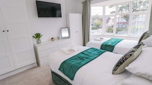 A hotel room with two beds, a TV, a mirror, a dresser, and a window with a view of houses.