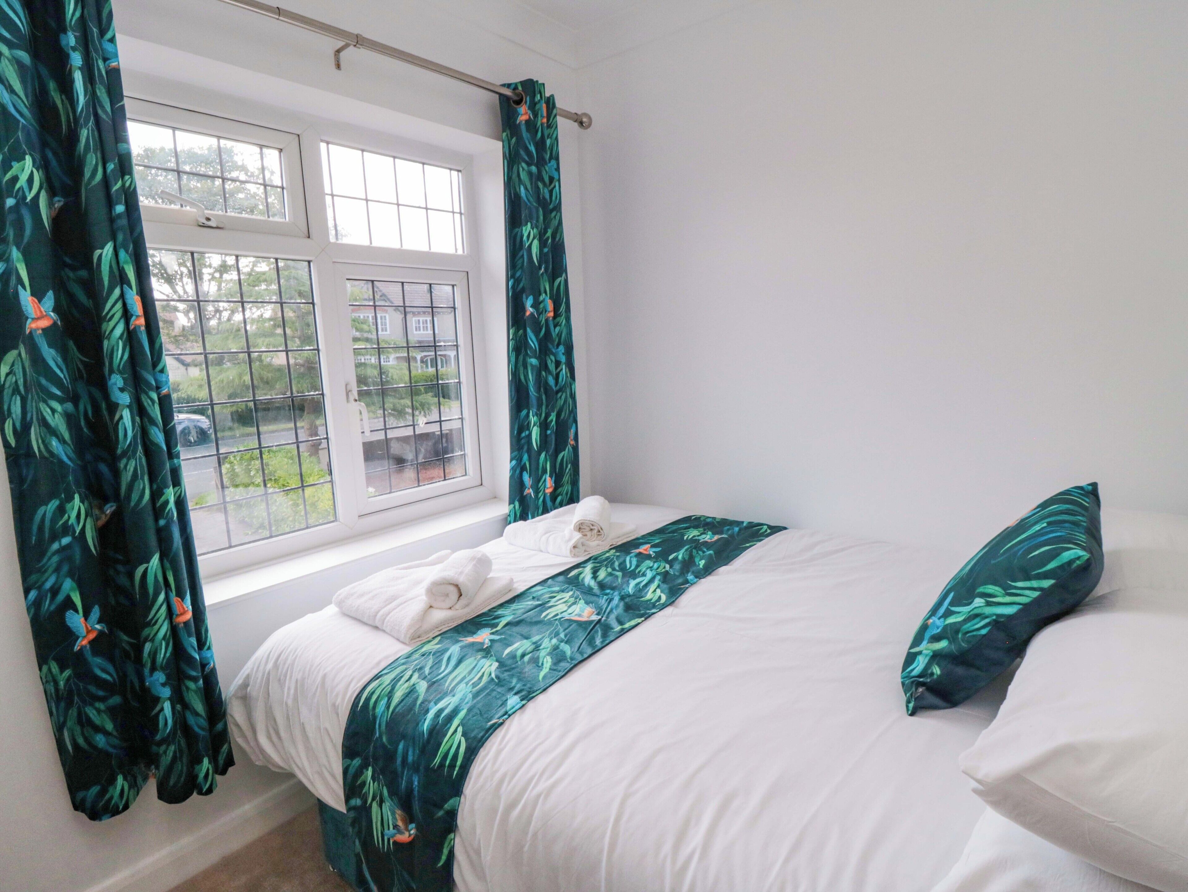 A bedroom with a bed, white bedding, a window with curtains, and a view of the outside.