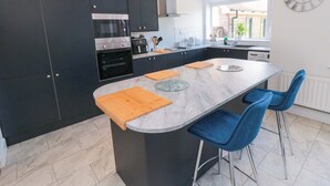 A modern kitchen with dark cabinets, a central island with bar stools, and a large wall clock.