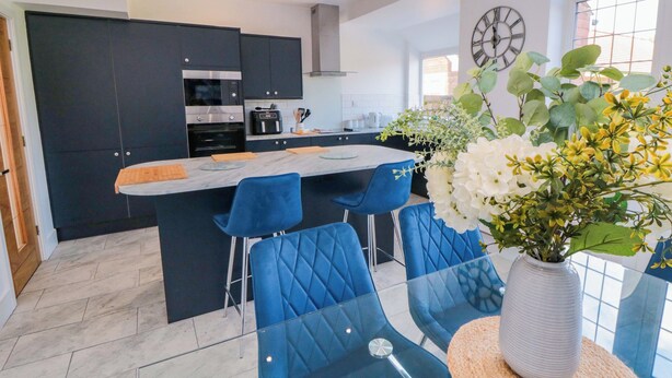 A modern kitchen with dark cabinets, a central island, and blue chairs.