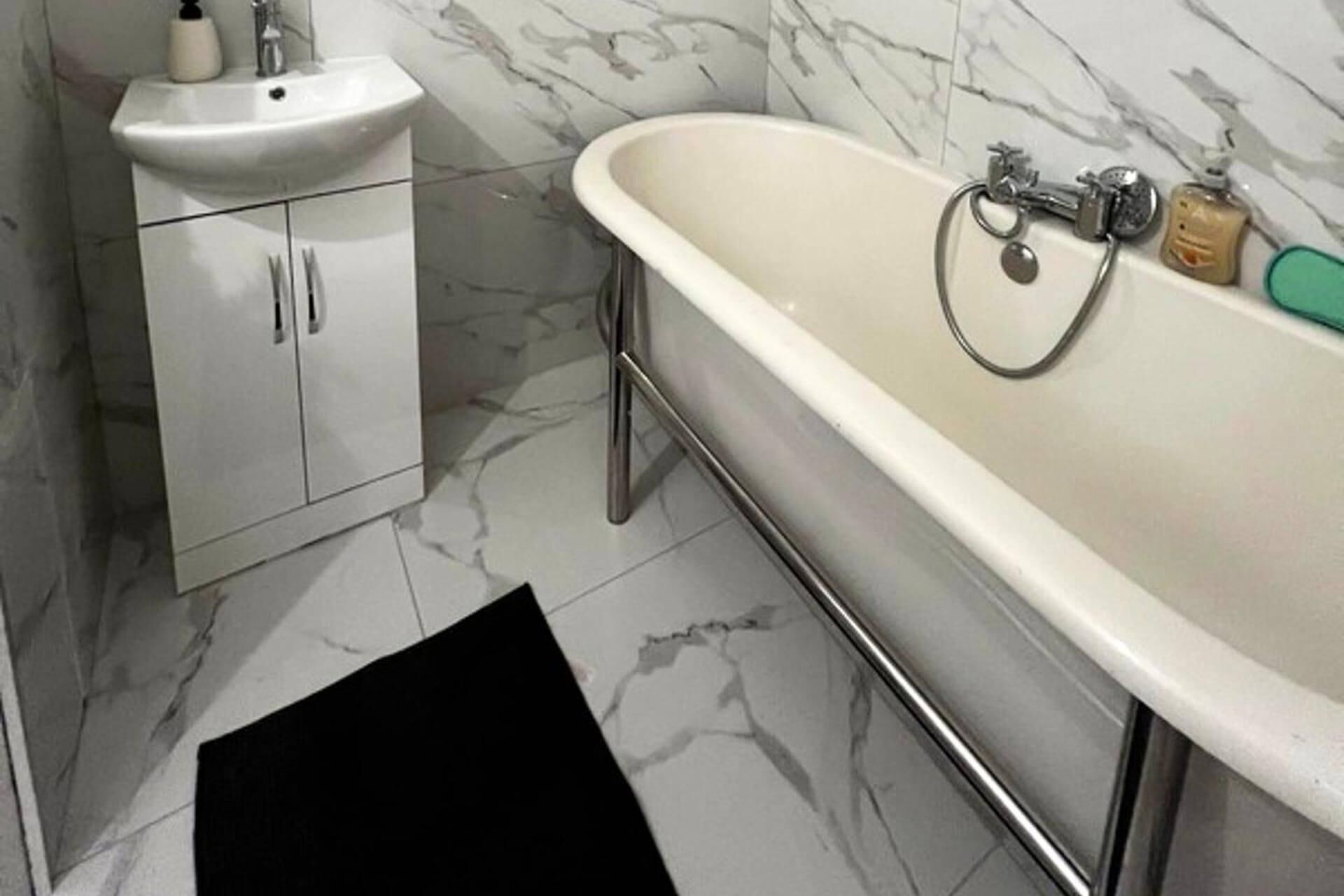 Une salle de bain avec un lavabo blanc, une baignoire et un tapis noir sur le sol.