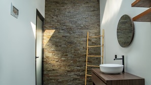 A bathroom with a stone wall, a wooden ladder, a white sink, and a wooden vanity. - The Moringa Bukit Villas (Kutuh)