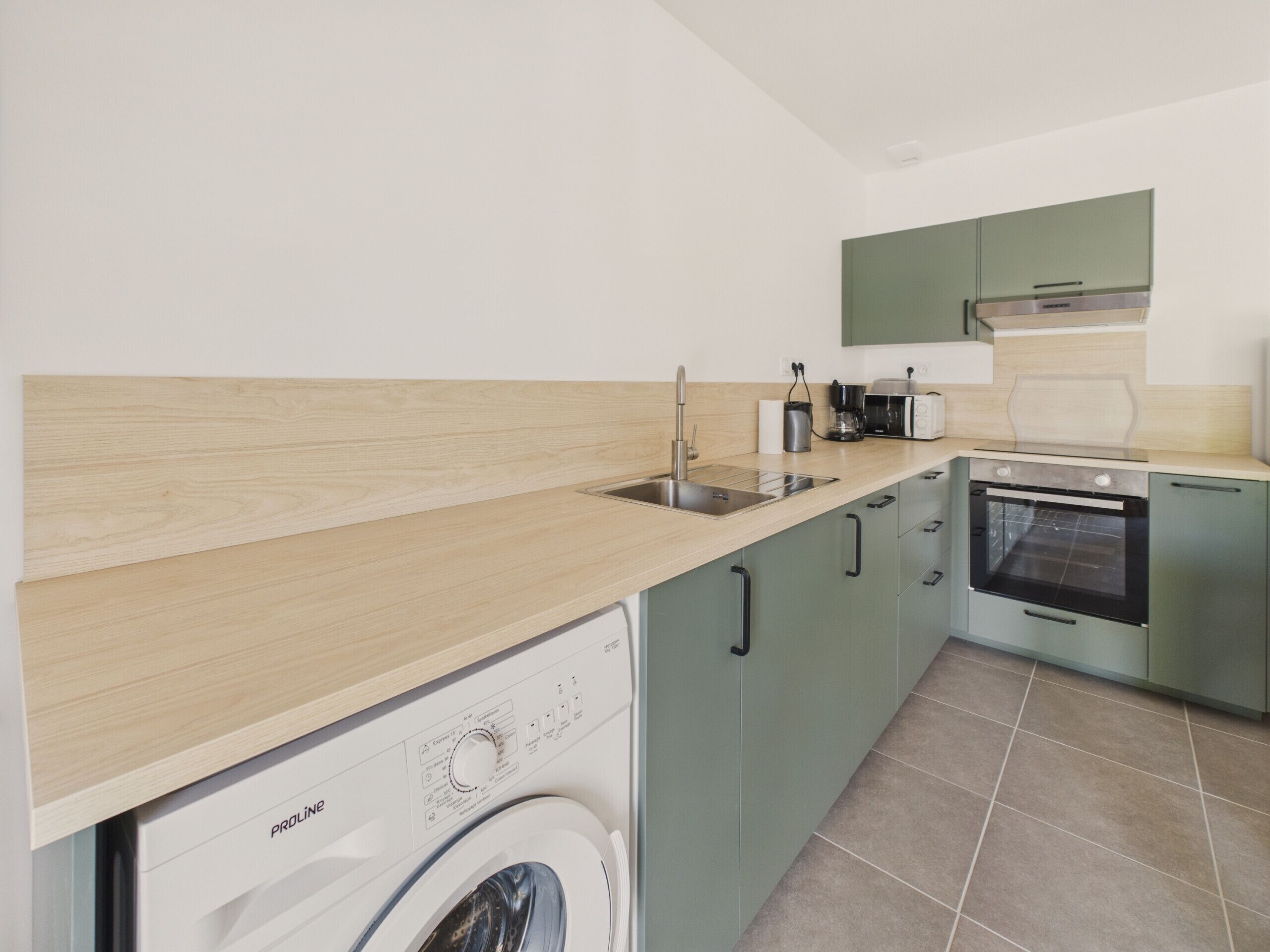 Een functionele keuken met een wasmachine, een spoelbak, een magnetron en een inbouwoven.