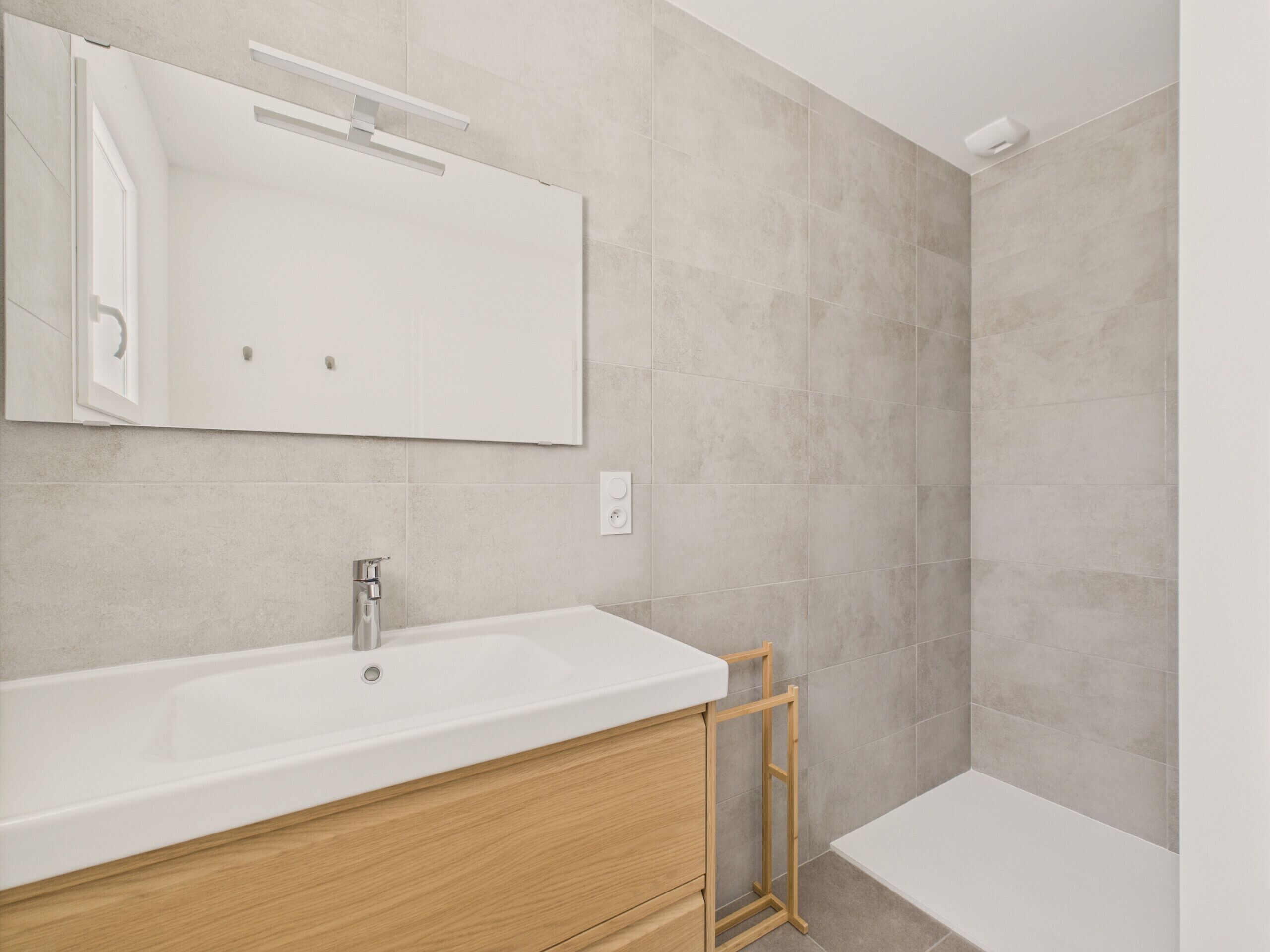 A modern bathroom with a large white sink, wooden vanity, and a mirror.