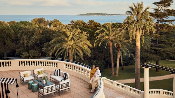 A terrace with outdoor furniture, a view of the sea, and palm trees. - COMO Le Beauvallon (Grimaud)