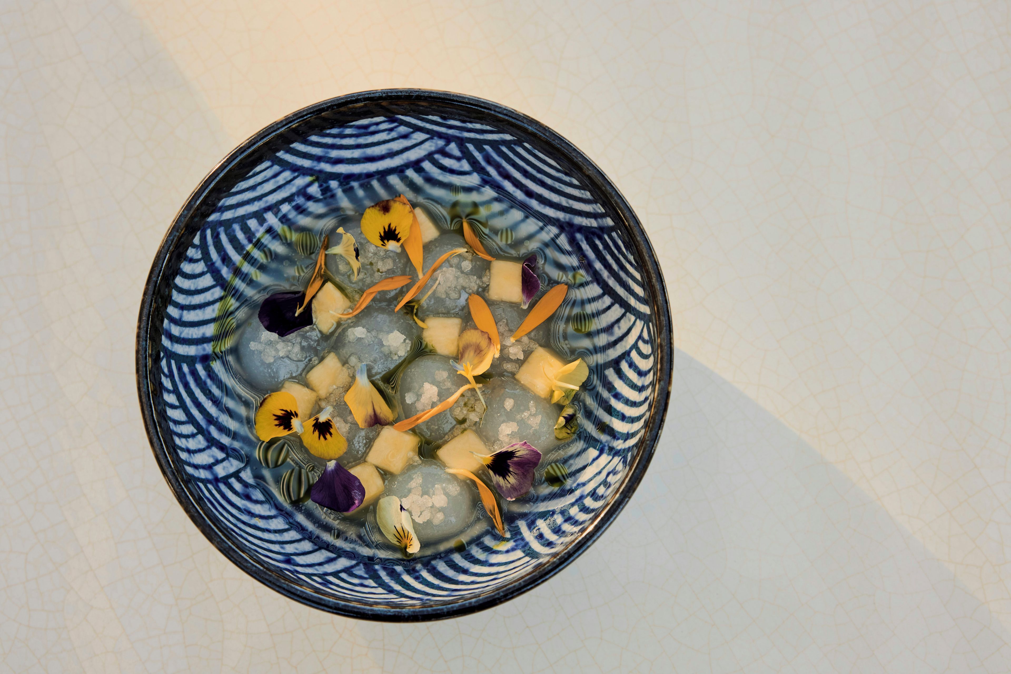 A bowl with ice cubes and various flower petals.