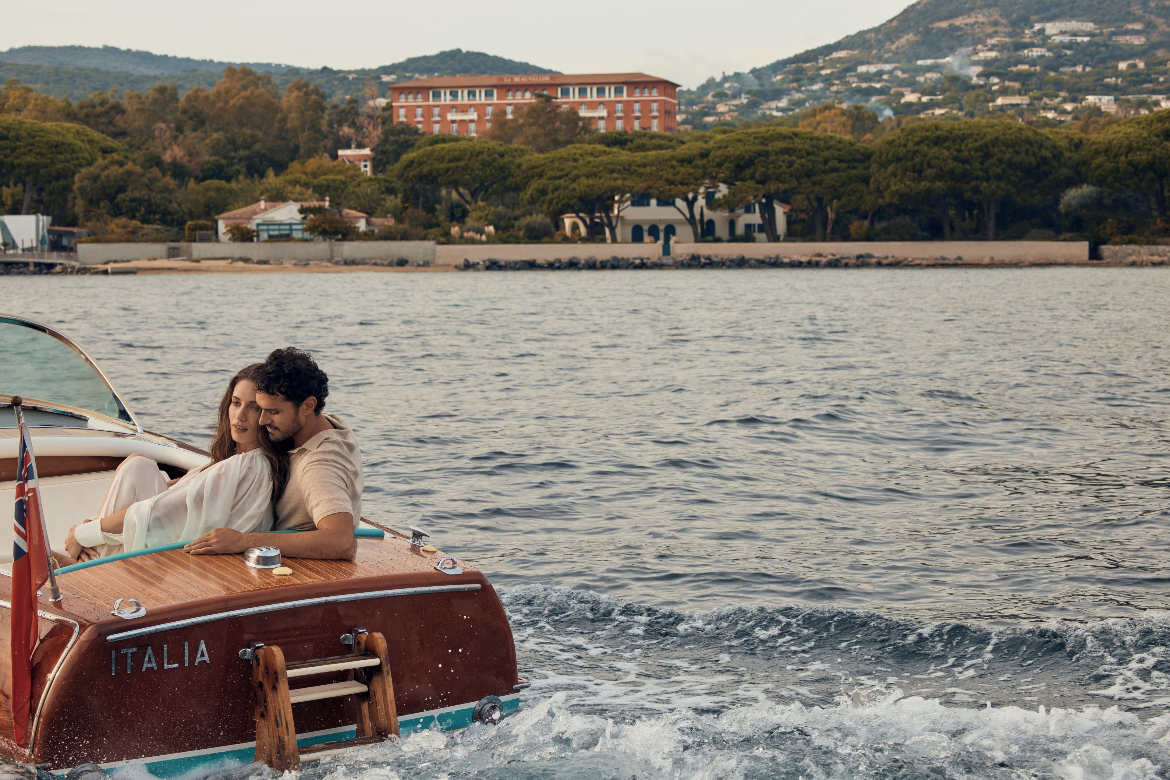Um barco com o nome 'ITALIA' na lateral, navegando em águas com edifícios e colinas ao fundo.
