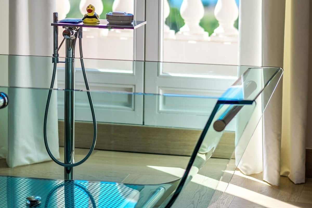 Une table en verre avec un pied en métal, une petite étagère sur laquelle se trouvent un canard en caoutchouc et un bol, et une vue sur la plage par la fenêtre.