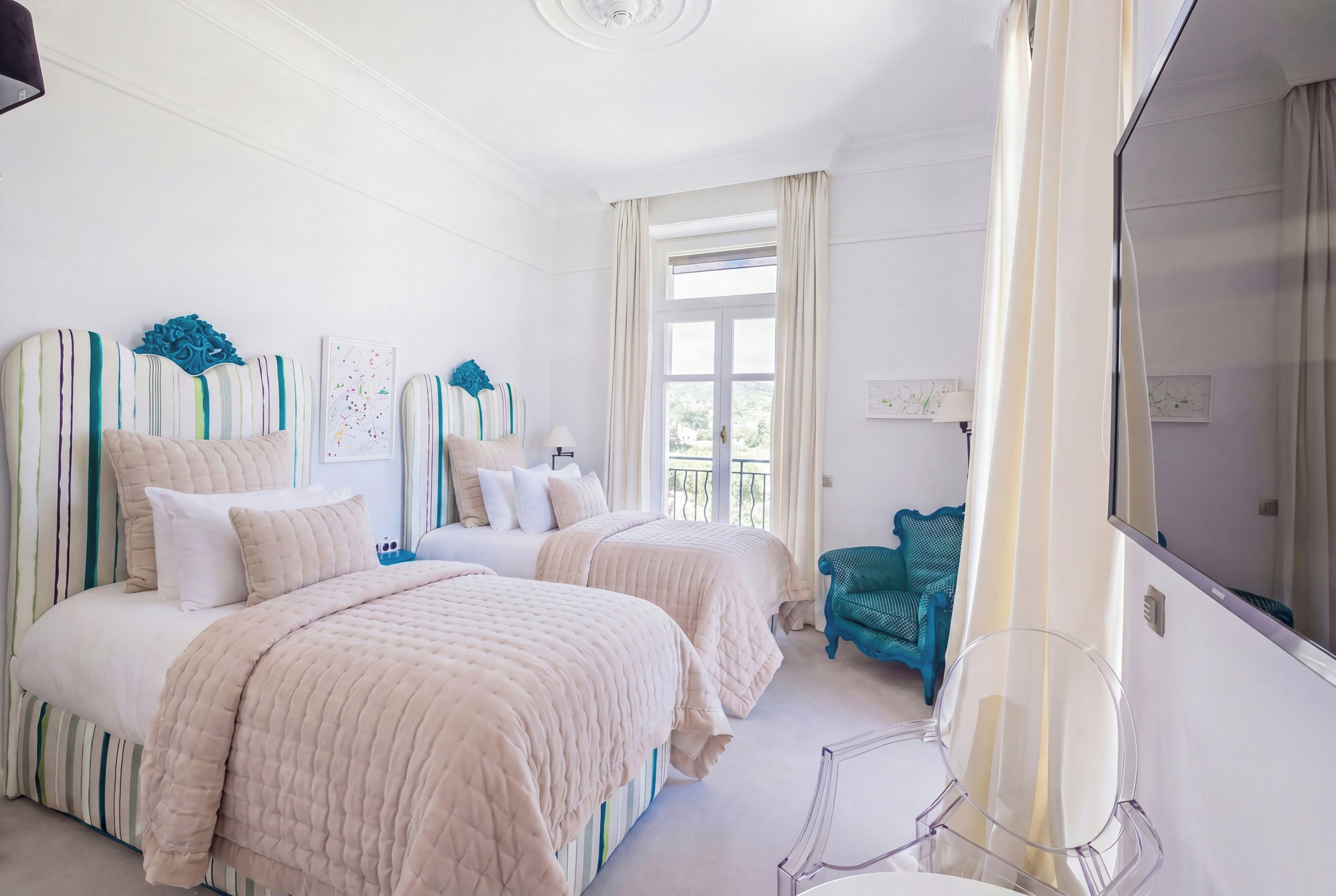 Ein Hotelzimmer mit zwei Betten, einem Fernseher, einem Sessel und einem fensterbepflanzten Fenster.