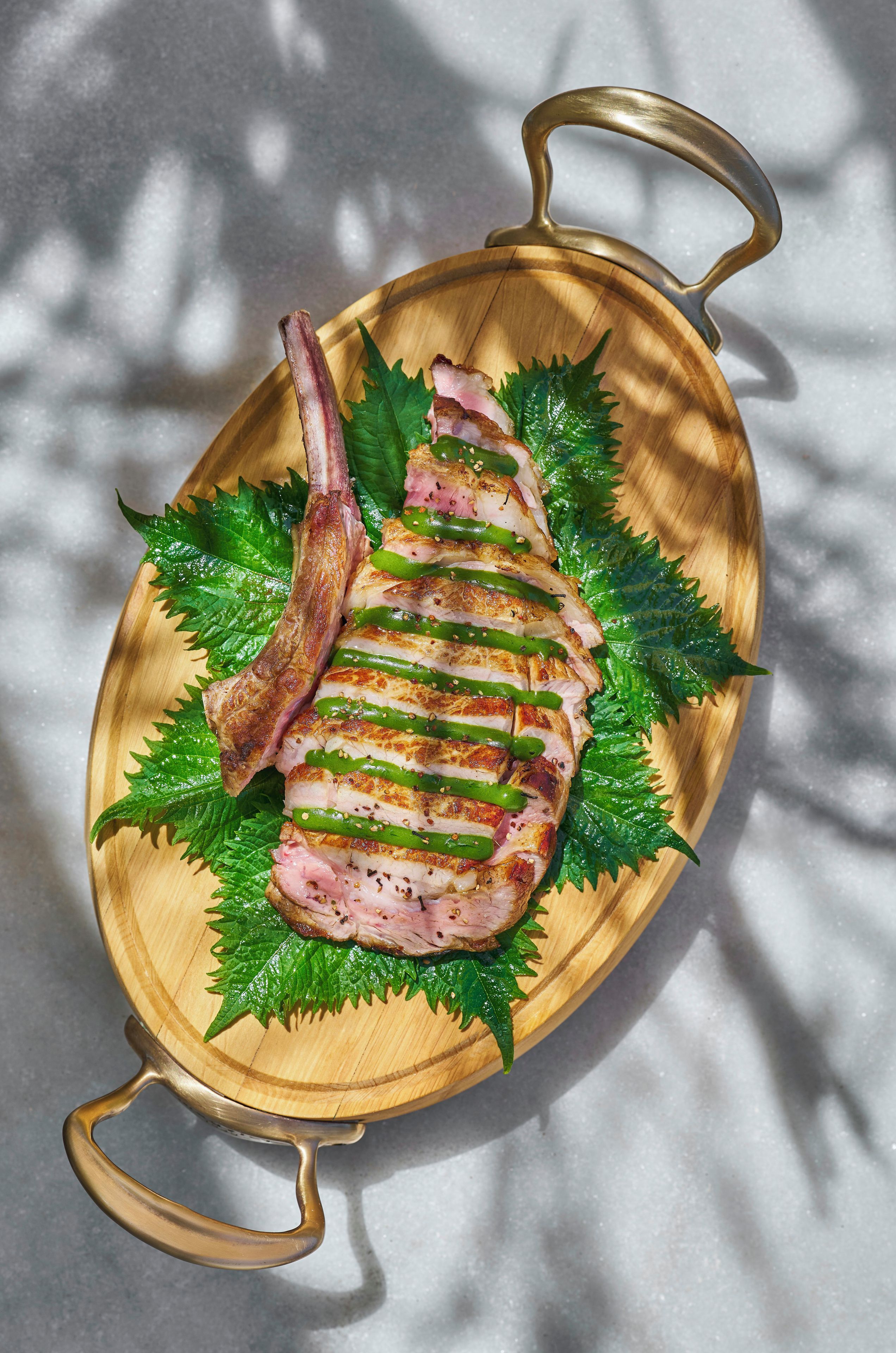 A wooden serving tray with a roasted duck and green leaves.