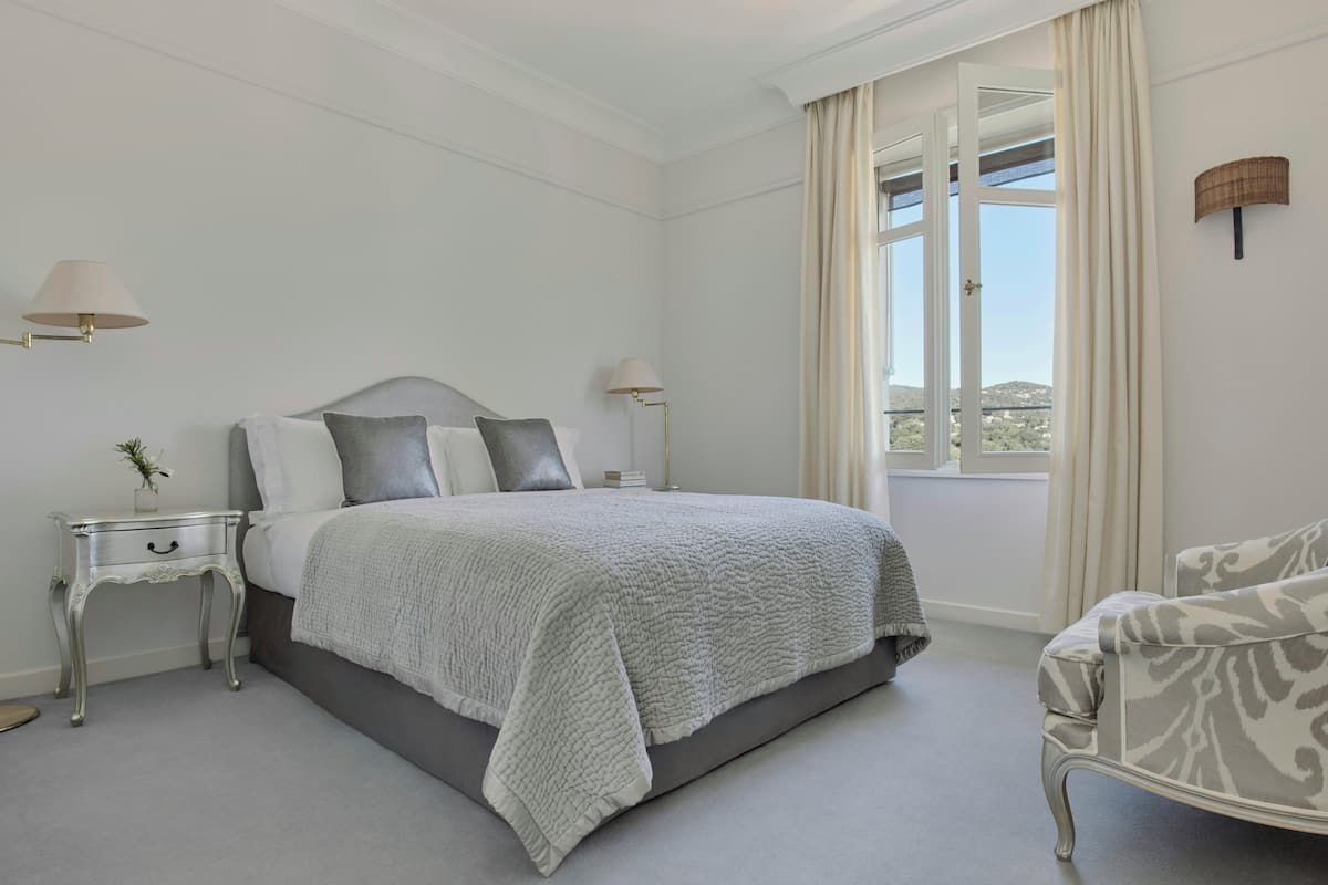 Une chambre à coucher avec un lit, des tables de chevet, une chaise et une fenêtre avec des rideaux.