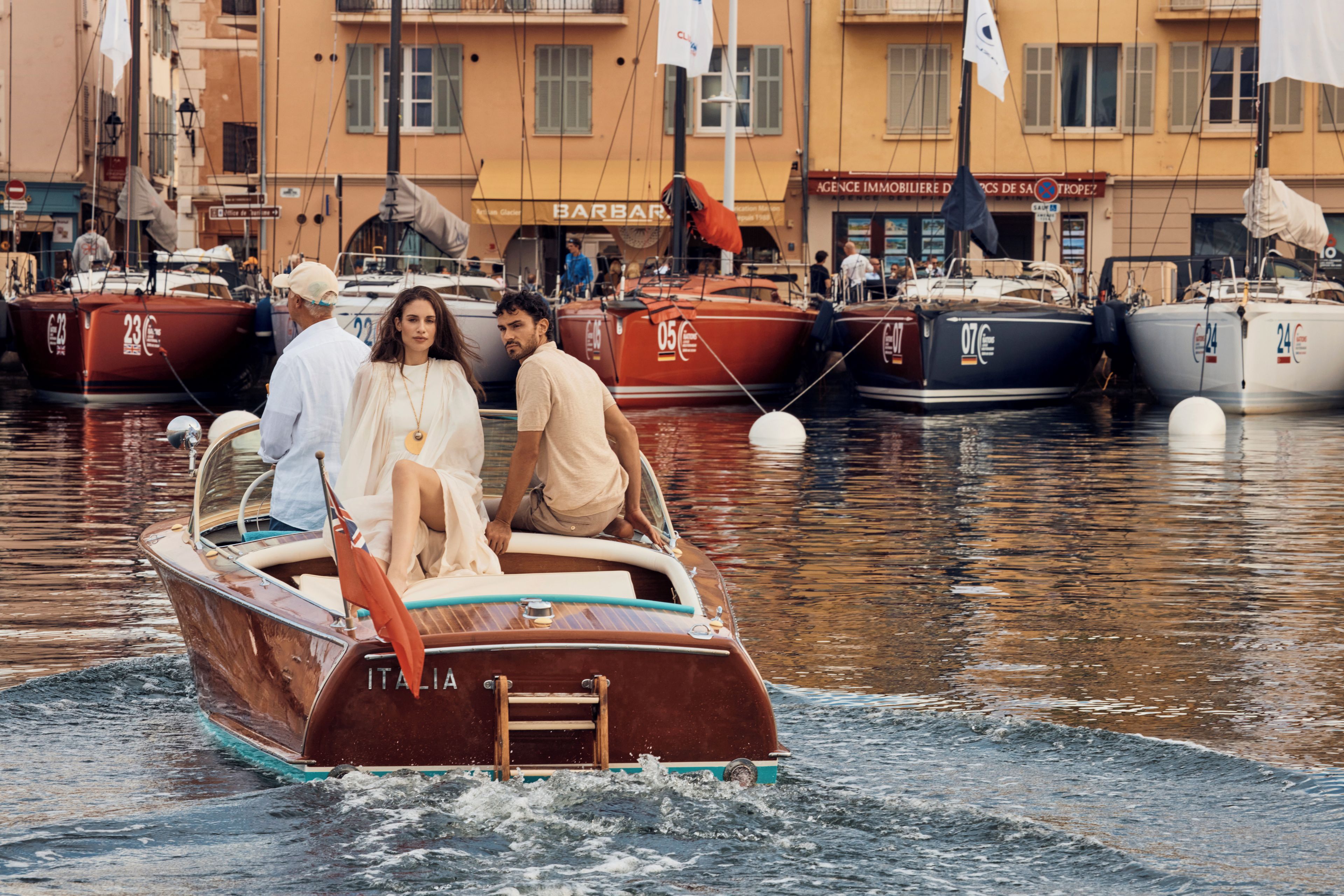 Ein Boot mit Passagieren liegt in einer Marina festgemacht, im Hintergrund sind weitere Boote und Gebäude zu sehen.