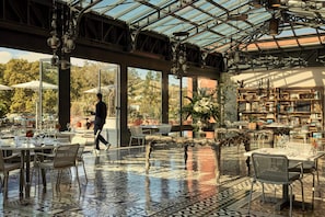 An indoor dining area with a glass ceiling, patterned floor, and a waiter walking. - COMO Le Beauvallon (Grimaud)